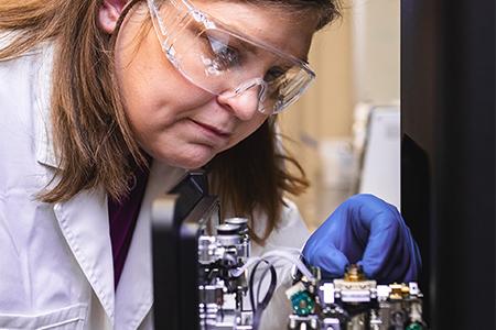 K-State nano-entomologist Amie Norton, left, places a stub containing a red flour beetle treated with micro eggshell particles, shown enlarged at right, into a scanning electron microscope in order to get an image of the particles that are present on the beetle.
